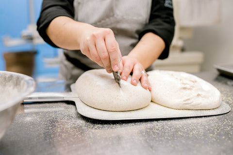 2 loaves of sourdough bread being scored down the center by Chef Anita